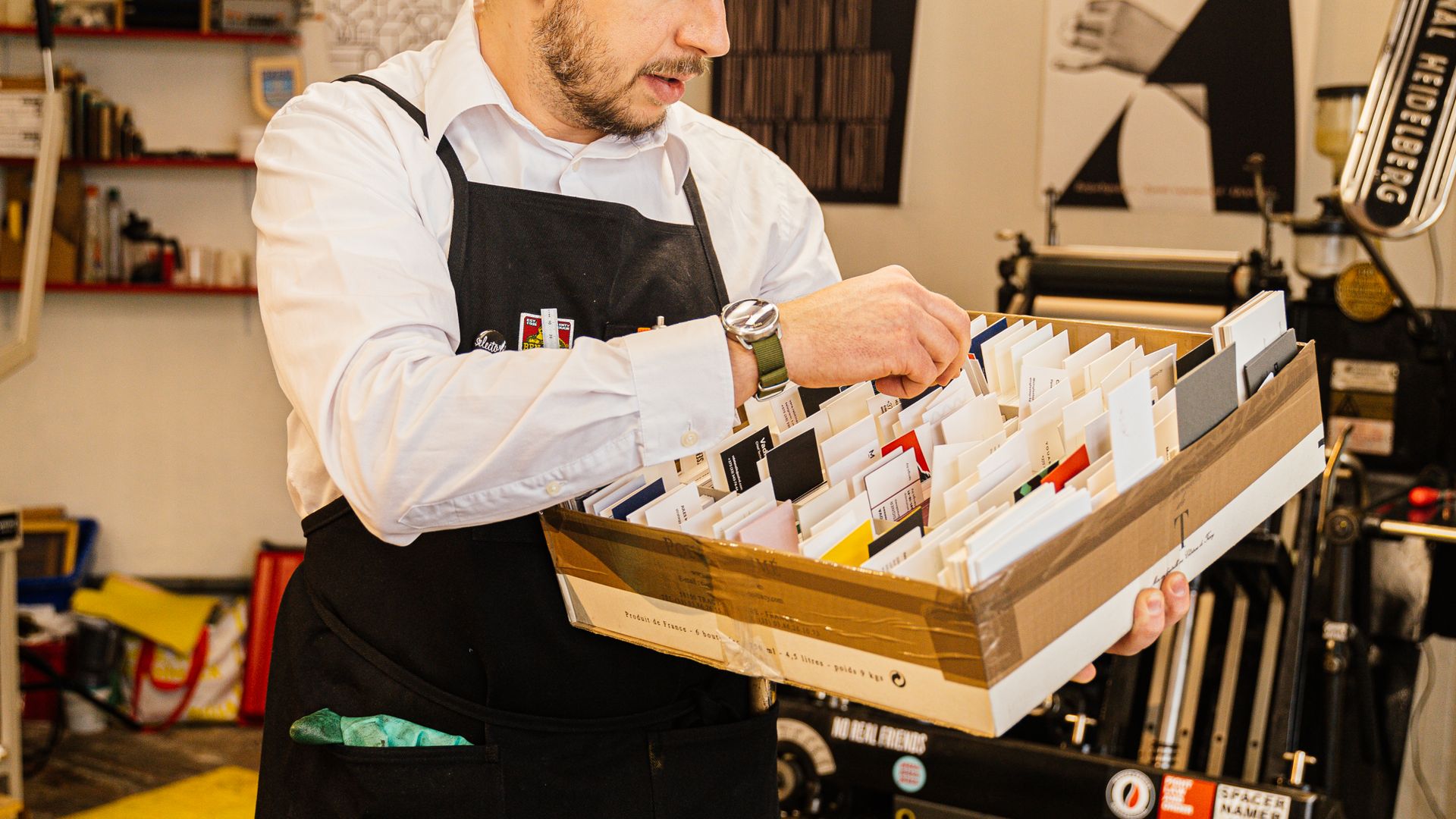 Print shop worker carrying a tray of organized paper samples in a workshop